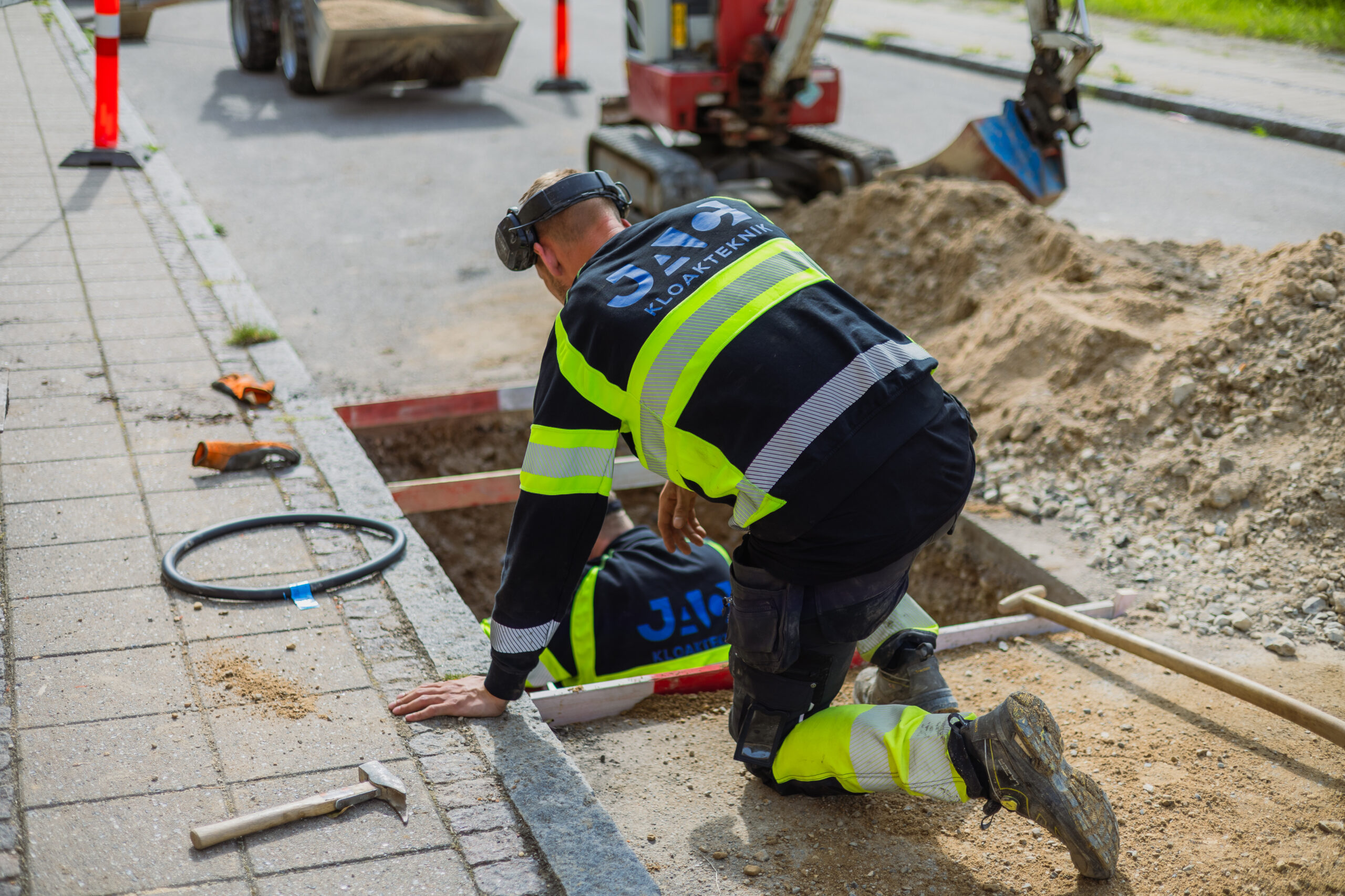 To JAC kloakarbejdere arbejder i udgravning ved vej og fortov under kloakprojekt.